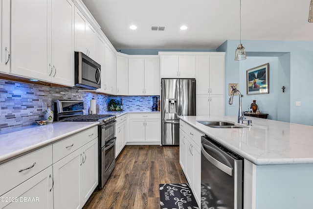 kitchen featuring appliances with stainless steel finishes, sink, white cabinetry, hanging light fixtures, and a kitchen island with sink