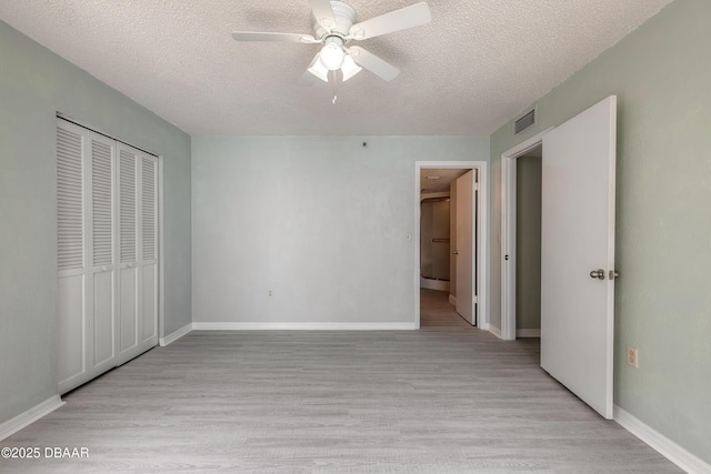 unfurnished bedroom featuring light wood-style floors, a textured ceiling, visible vents, and a closet
