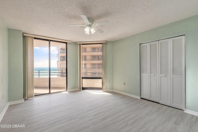 unfurnished bedroom with floor to ceiling windows, a textured ceiling, wood finished floors, a water view, and access to outside