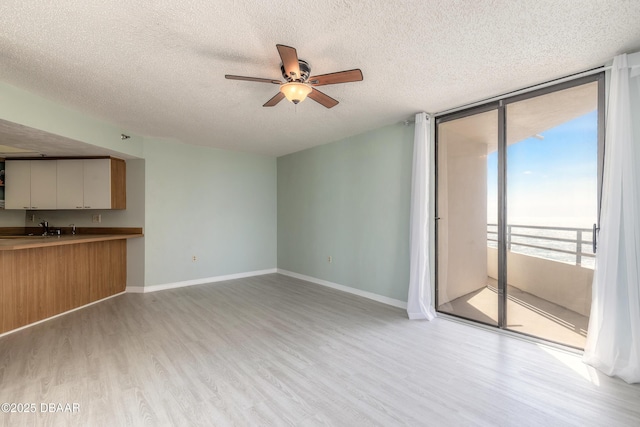 unfurnished living room featuring light wood-type flooring, a textured ceiling, ceiling fan, and baseboards