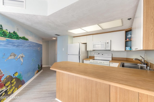 kitchen with a peninsula, white appliances, white cabinetry, a sink, and light wood finished floors