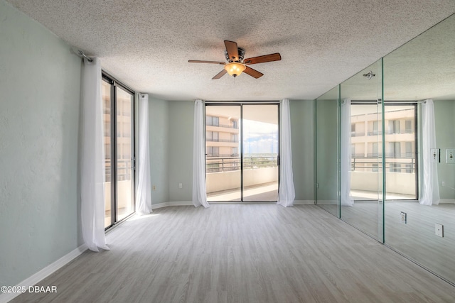 empty room with a ceiling fan, a textured ceiling, wood finished floors, and a wall of windows