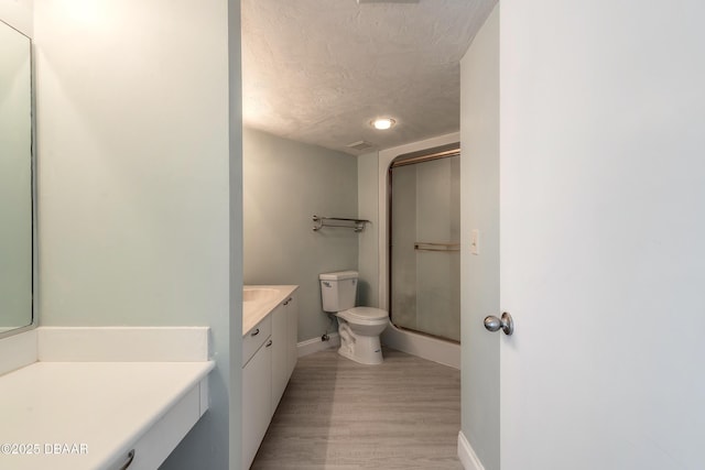 full bath featuring vanity, a shower with door, wood finished floors, toilet, and baseboards
