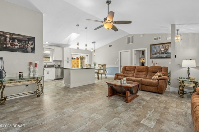 living area with visible vents, a ceiling fan, light wood-type flooring, vaulted ceiling with skylight, and baseboards