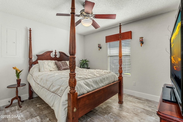 bedroom featuring electric panel, a textured ceiling, baseboards, and wood finished floors