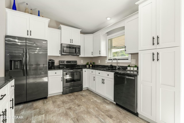 kitchen with a sink, white cabinetry, appliances with stainless steel finishes, light wood finished floors, and dark stone countertops