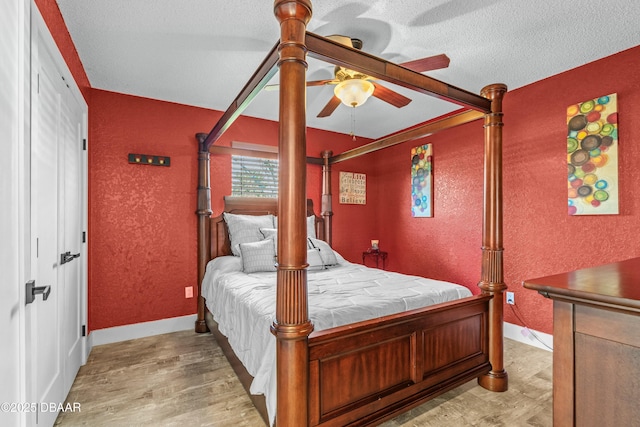 bedroom with a textured ceiling, a textured wall, light wood finished floors, and baseboards