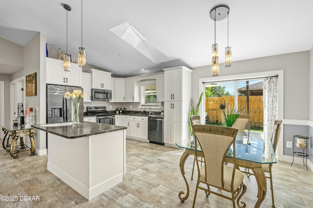 kitchen featuring white cabinets, appliances with stainless steel finishes, a center island, lofted ceiling with skylight, and dark countertops