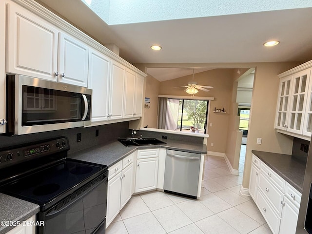 kitchen with appliances with stainless steel finishes, a peninsula, dark countertops, lofted ceiling, and a sink