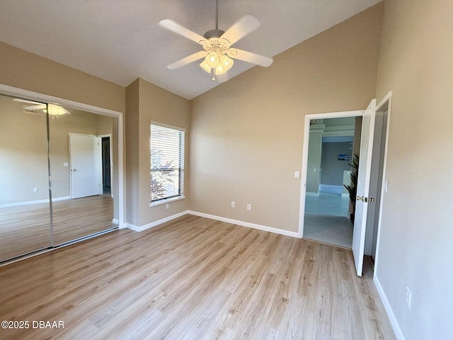 unfurnished bedroom featuring a closet, baseboards, light wood-type flooring, a ceiling fan, and high vaulted ceiling