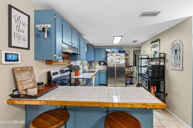343 Lake Como Dr, Pomona Park, FL 32181 - kitchen with stainless steel appliances, blue cabinets, under cabinet range hood, and light tile patterned floors