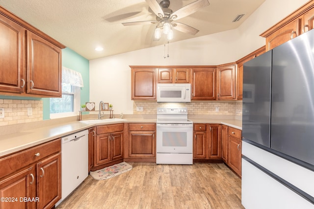 kitchen featuring decorative backsplash, white appliances, sink, light hardwood / wood-style flooring, and lofted ceiling