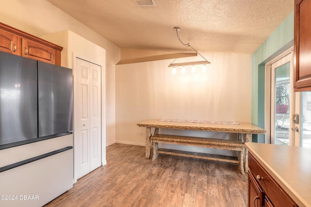 dining area featuring a textured ceiling, light hardwood / wood-style flooring, and vaulted ceiling