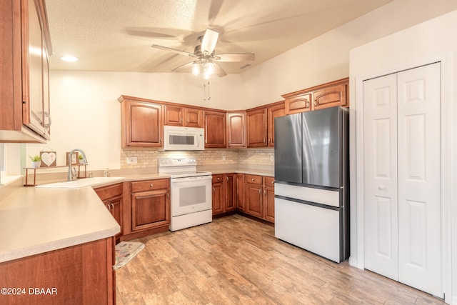 kitchen with sink, vaulted ceiling, a textured ceiling, white appliances, and light wood-type flooring