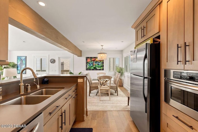 kitchen with appliances with stainless steel finishes, recessed lighting, hanging light fixtures, a sink, and light wood-type flooring