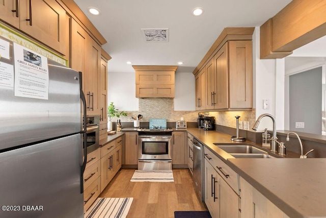 kitchen featuring light wood finished floors, a sink, stainless steel appliances, tasteful backsplash, and recessed lighting