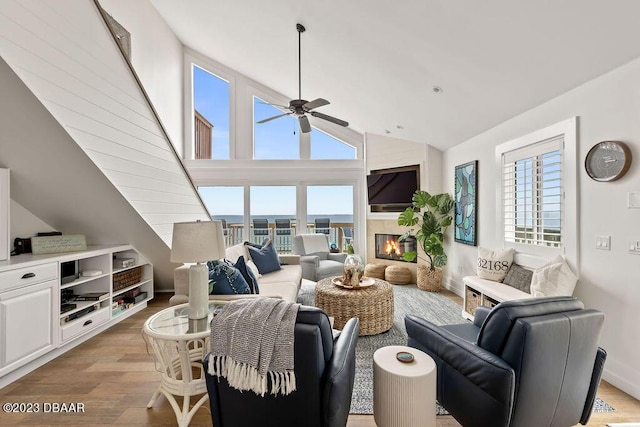 living room featuring a tile fireplace, light wood-style flooring, ceiling fan, and vaulted ceiling