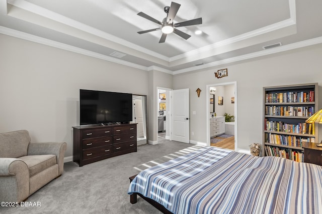 bedroom featuring light colored carpet, ornamental molding, a tray ceiling, and ensuite bath