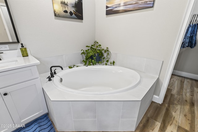 bathroom featuring a relaxing tiled tub, vanity, and wood-type flooring