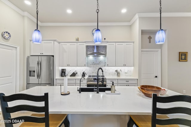 kitchen featuring wall chimney exhaust hood, stainless steel appliances, decorative light fixtures, and an island with sink