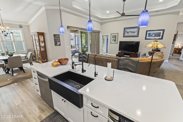 kitchen with sink, white cabinetry, decorative light fixtures, stainless steel dishwasher, and a tray ceiling