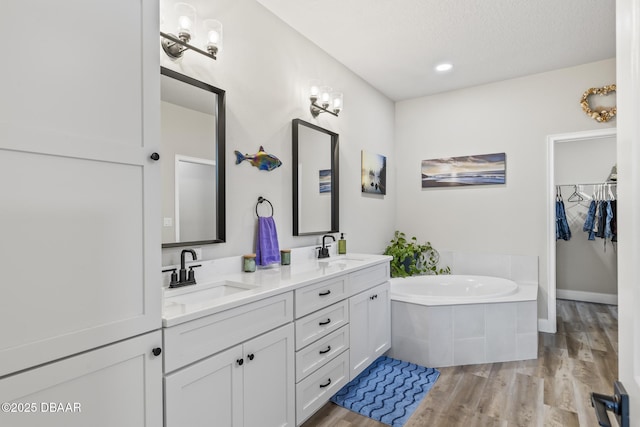 bathroom with hardwood / wood-style flooring, vanity, tiled bath, and a textured ceiling