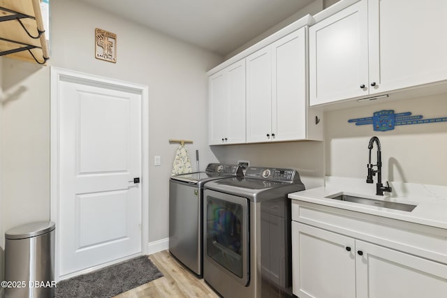 laundry area with washer and dryer, sink, cabinets, and light hardwood / wood-style flooring