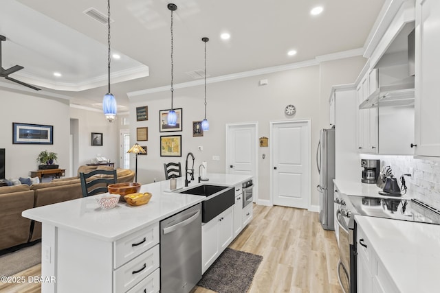 kitchen with appliances with stainless steel finishes, white cabinetry, hanging light fixtures, a kitchen island with sink, and a raised ceiling