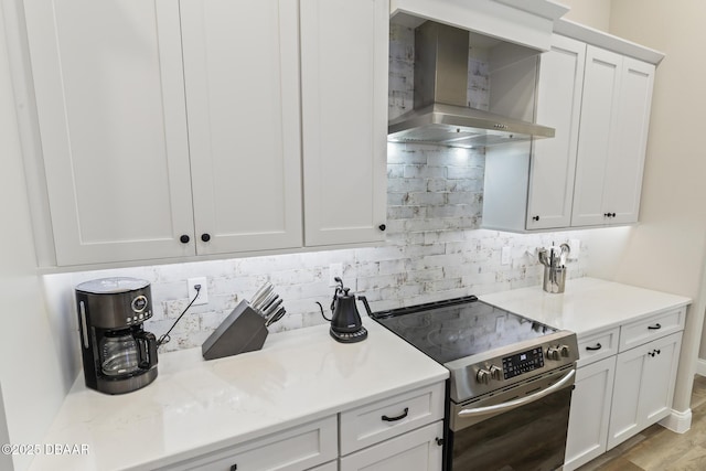 kitchen with stainless steel electric range, decorative backsplash, white cabinets, and wall chimney exhaust hood