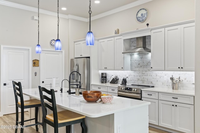 kitchen featuring white cabinetry, hanging light fixtures, appliances with stainless steel finishes, a kitchen island with sink, and wall chimney range hood