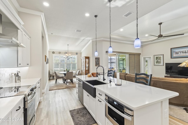 kitchen featuring appliances with stainless steel finishes, decorative light fixtures, sink, white cabinets, and a center island with sink