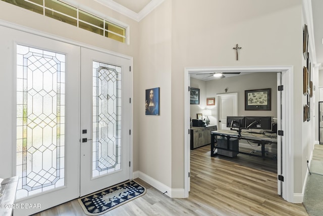 entryway featuring light hardwood / wood-style flooring, ceiling fan, a towering ceiling, ornamental molding, and french doors