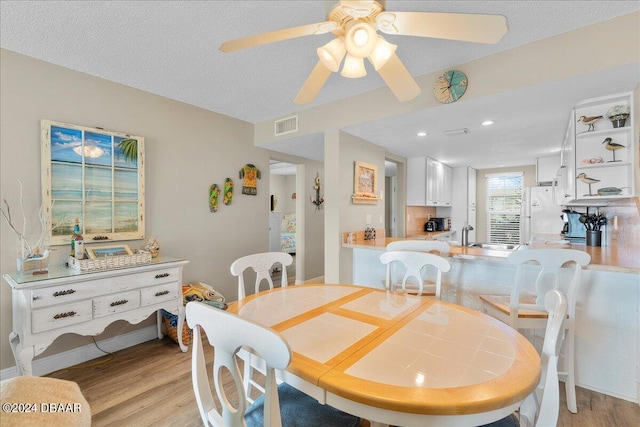 dining area with light hardwood / wood-style flooring, a textured ceiling, and ceiling fan