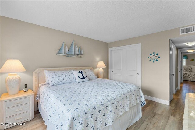 bedroom with light hardwood / wood-style floors, a textured ceiling, and a closet