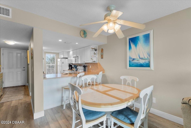 dining space with ceiling fan, a textured ceiling, and light hardwood / wood-style floors