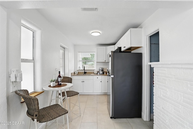 kitchen featuring a sink, light tile patterned floors, white cabinetry, visible vents, and freestanding refrigerator