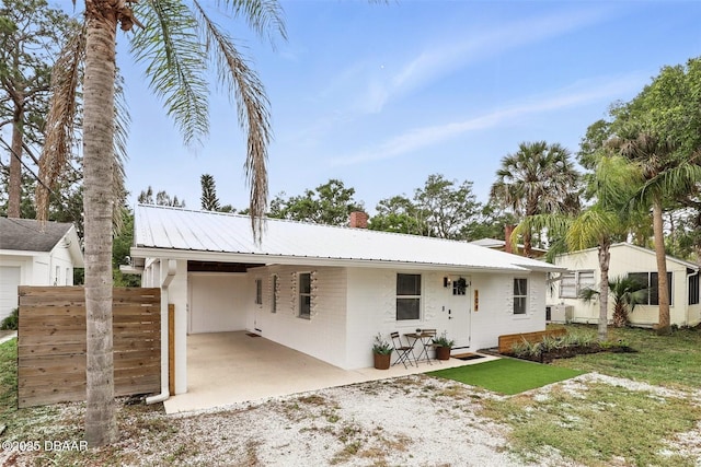 view of front facade featuring central AC unit, an attached carport, a chimney, fence, and gravel driveway