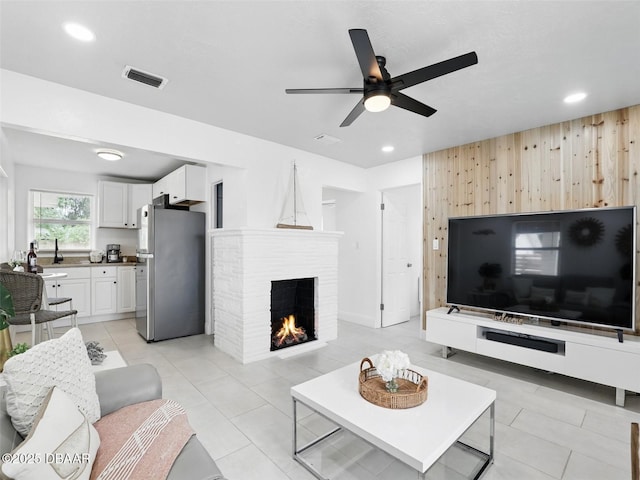 living area with visible vents, wood walls, ceiling fan, a fireplace, and light tile patterned floors