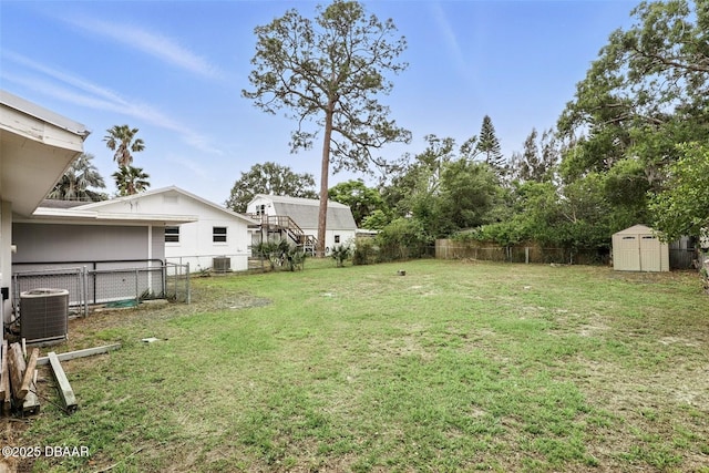 view of yard with a fenced backyard, central AC unit, an outdoor structure, and a storage unit
