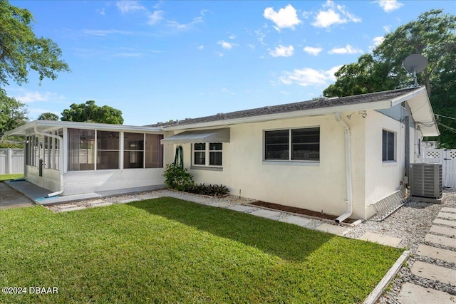 rear view of property with a sunroom, central AC, and a lawn