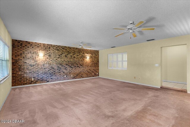 spare room featuring light carpet, plenty of natural light, and brick wall