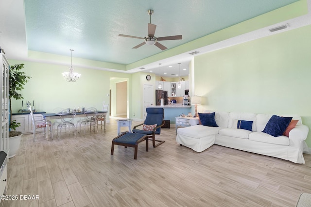 living room featuring a raised ceiling, light hardwood / wood-style flooring, ceiling fan with notable chandelier, and a textured ceiling