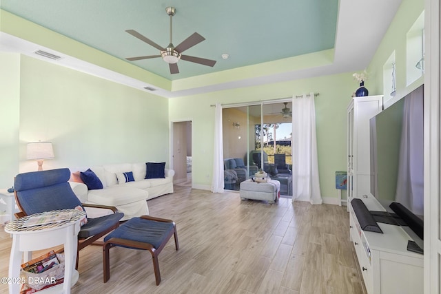 living room featuring light hardwood / wood-style floors, a raised ceiling, and ceiling fan