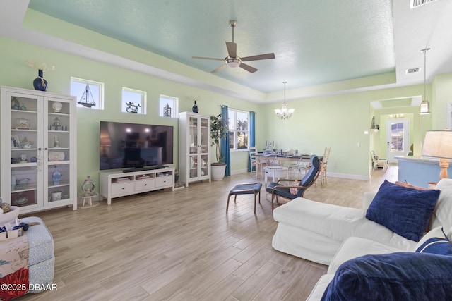 living room featuring ceiling fan with notable chandelier, a textured ceiling, light hardwood / wood-style flooring, and a raised ceiling