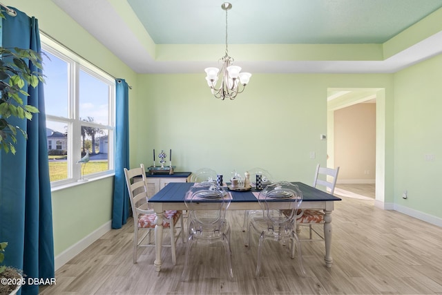 dining room featuring a raised ceiling, light wood-type flooring, and an inviting chandelier