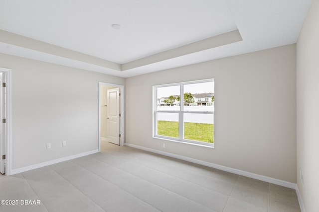 empty room featuring a raised ceiling and baseboards