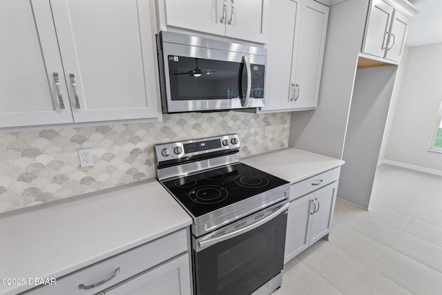 kitchen with baseboards, light countertops, light tile patterned floors, decorative backsplash, and stainless steel appliances