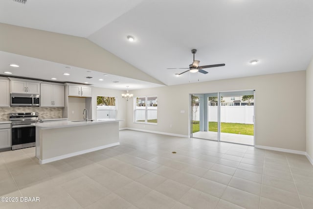 kitchen with ceiling fan with notable chandelier, open floor plan, appliances with stainless steel finishes, light countertops, and decorative backsplash