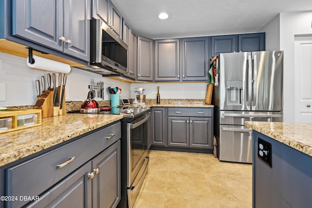 kitchen featuring light tile patterned flooring, appliances with stainless steel finishes, a textured ceiling, gray cabinets, and light stone countertops