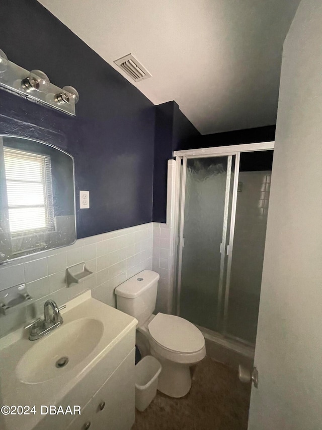 bathroom with tile walls, vanity, toilet, and a shower with shower door